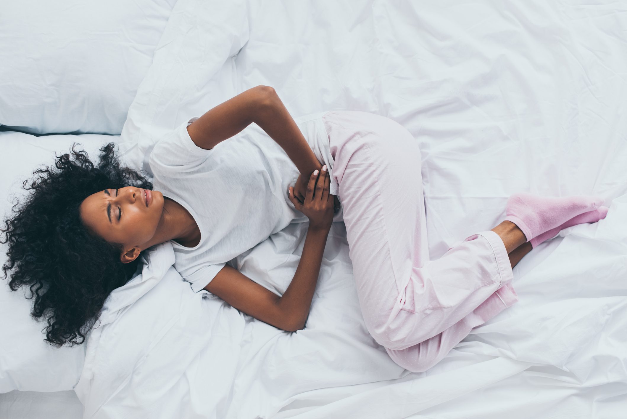 Woman lying on green sheets in discomfort with pillow over torso.